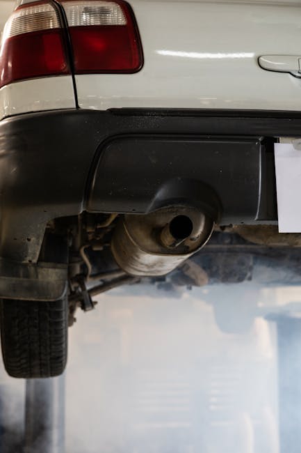 Close-up of a car's exhaust system emitting smoke in an auto repair shop setting.