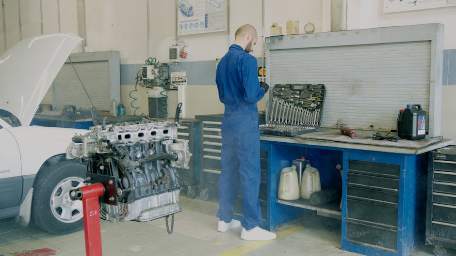 Mechanic in blue coveralls working on car engine in auto repair shop.