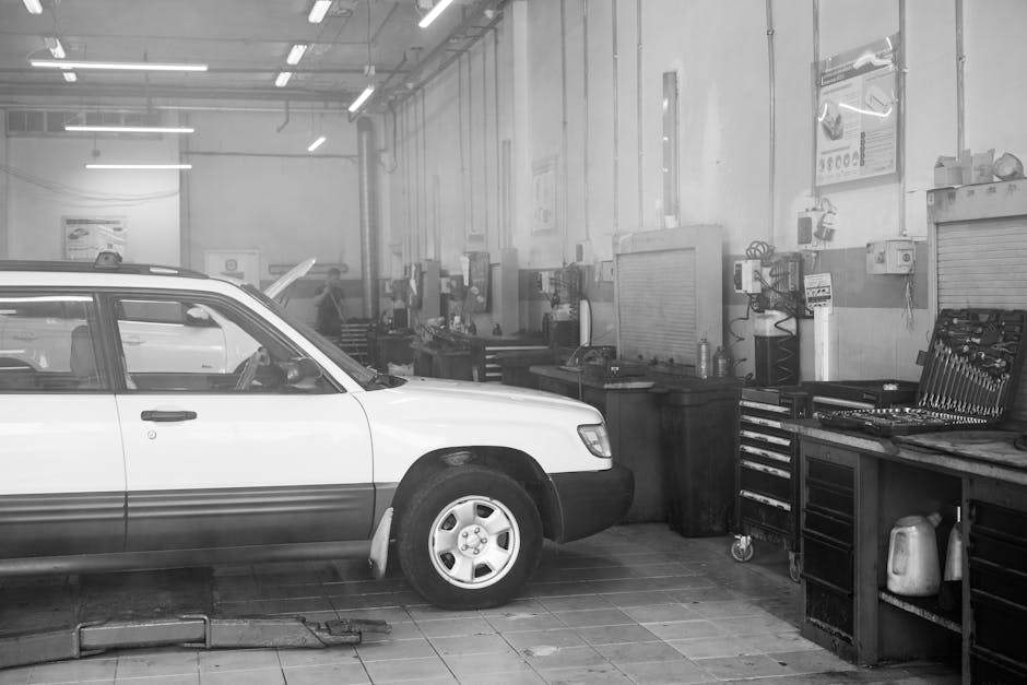 Black and white image of a car in a garage surrounded by tools and equipment.