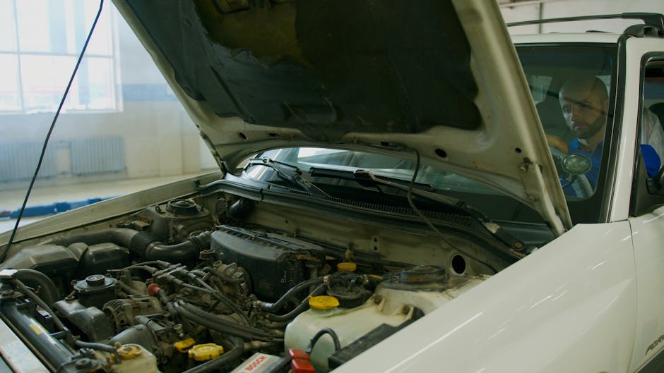 Mechanic checking car engine under open hood in a garage setting.