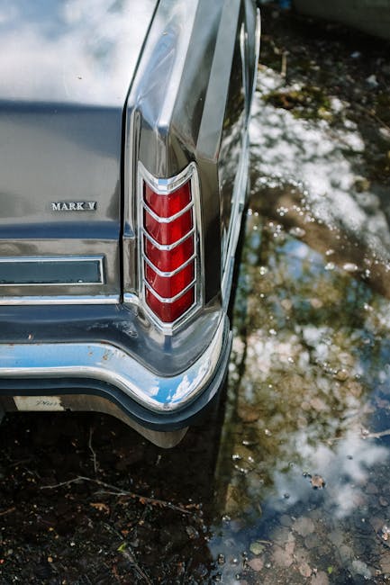 Close-up of a classic car's tail light with reflections on water, showcasing vintage style.